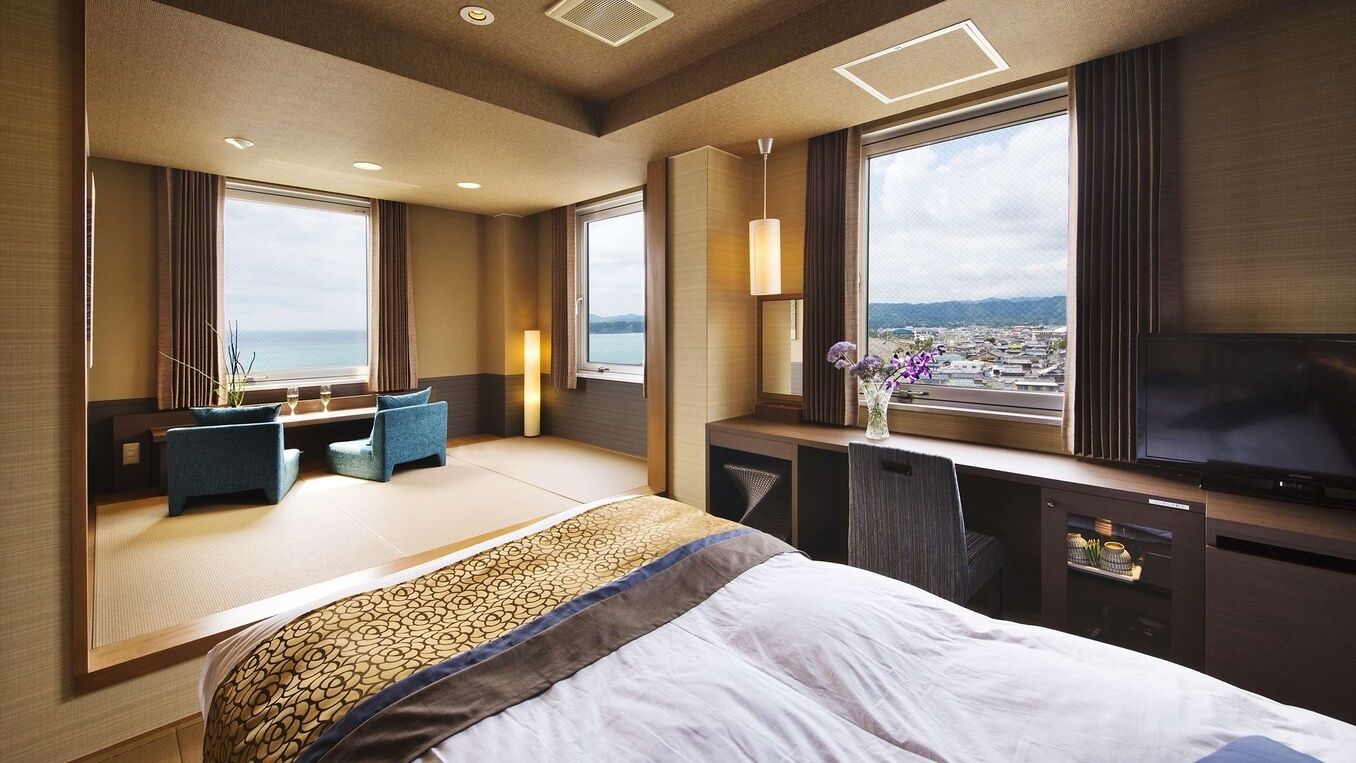 A hotel room with a bed, seating area, TV, and large windows with a view.