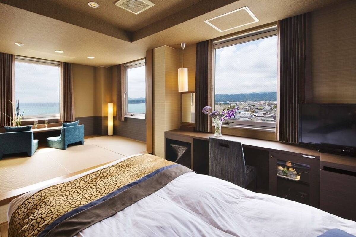 A hotel room with a bed, seating area, TV, and large windows with a view.