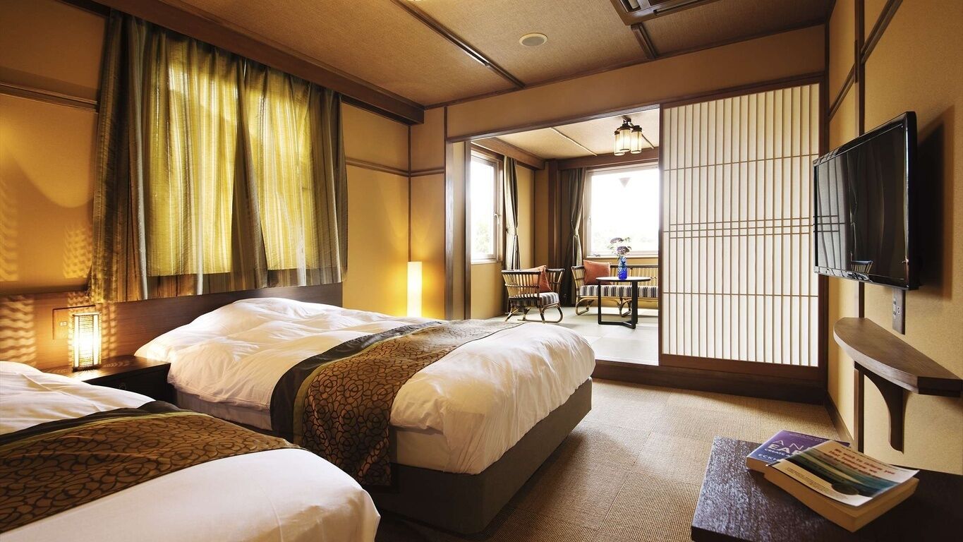 Habitación de hotel con dos camas, un televisor, una mesita con un libro y vistas a un balcón.