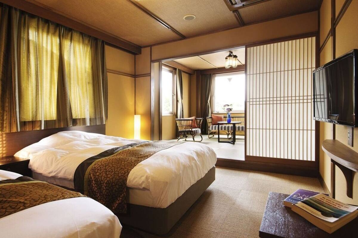 Habitación de hotel con dos camas, un televisor, una mesita con un libro y vistas a un balcón.