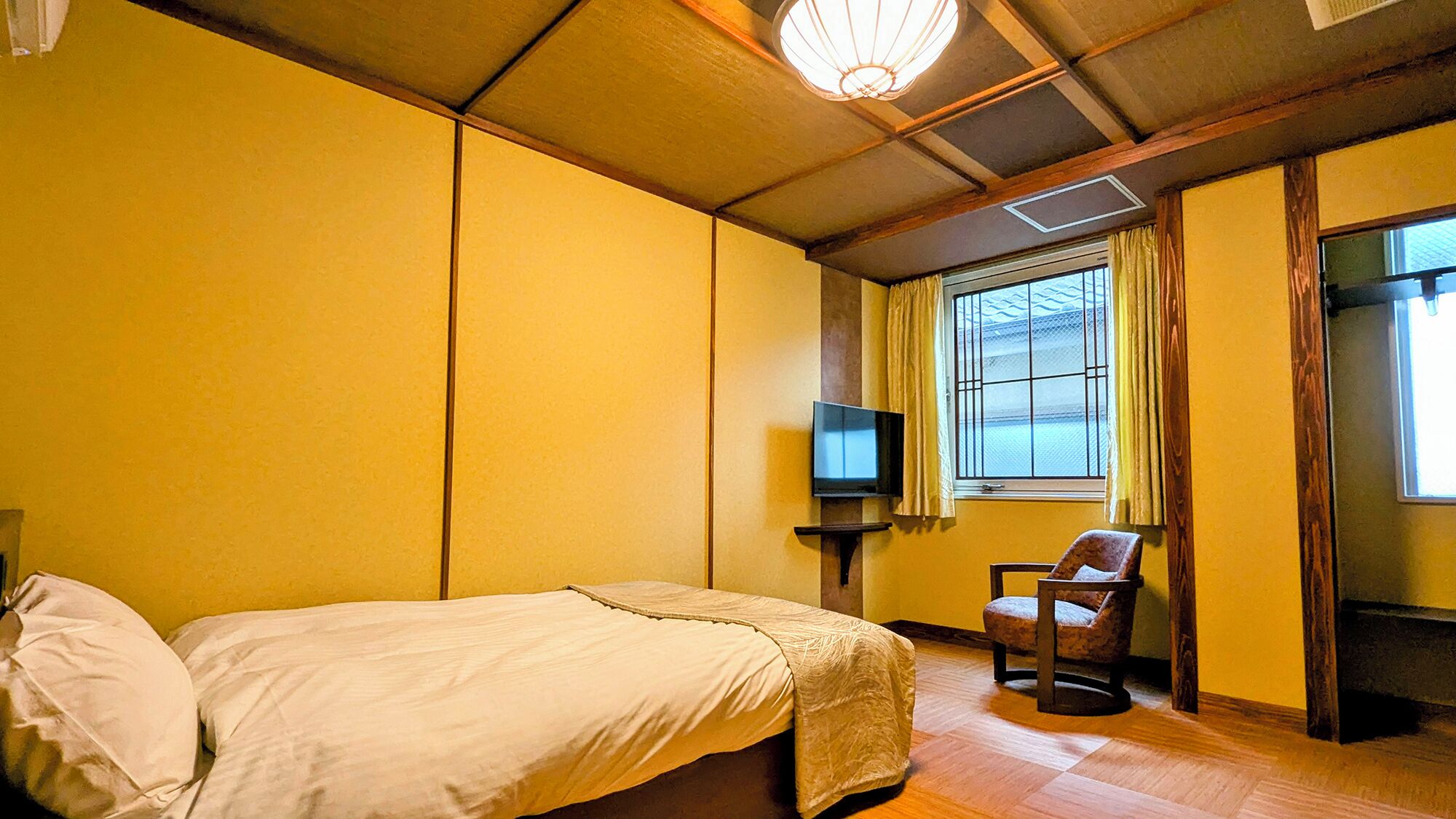 Una habitación con cama, silla, televisión y ventana con cortinas.