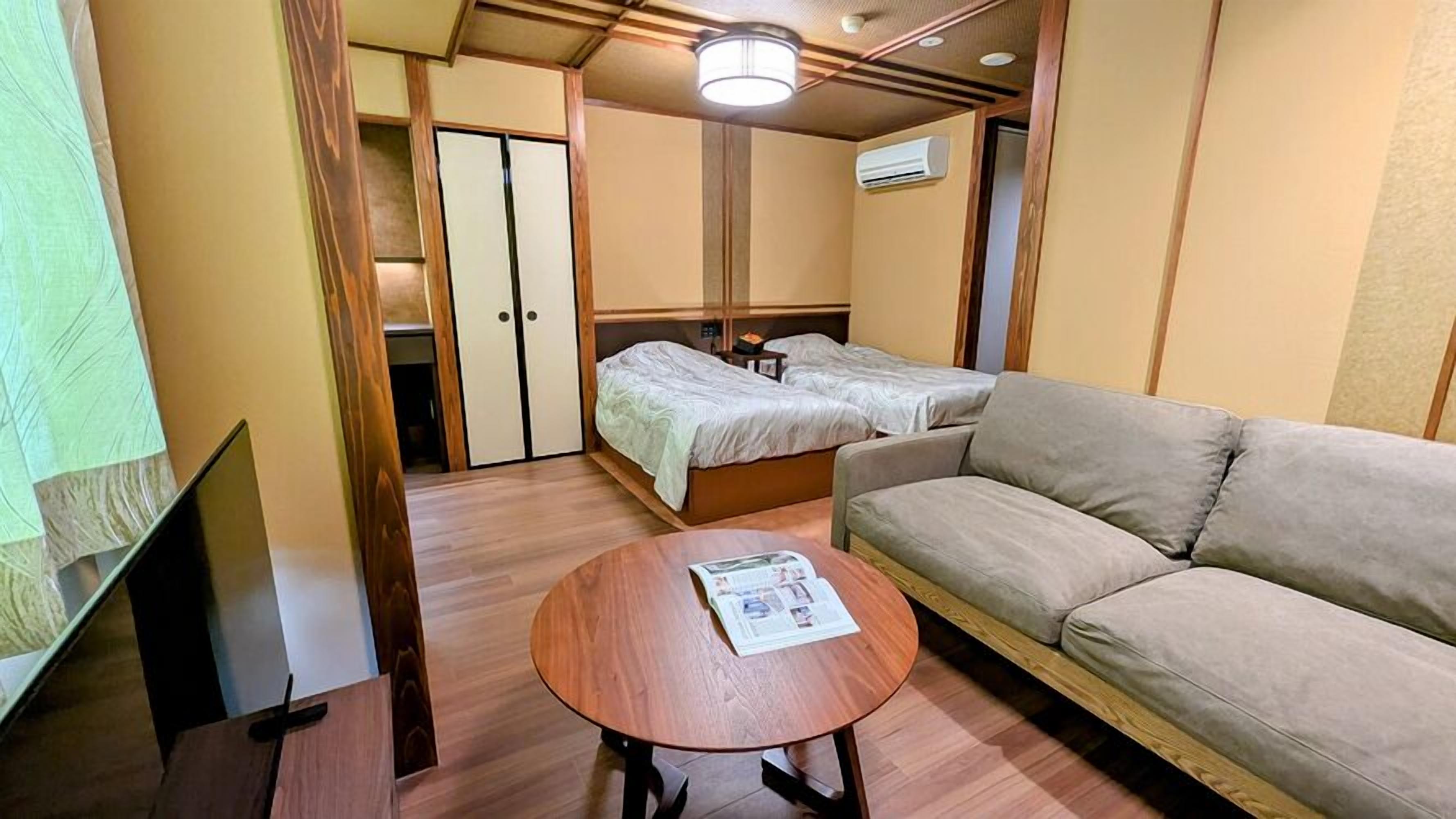 A hotel room with a bed, a sofa, a small table with a magazine, and a TV.