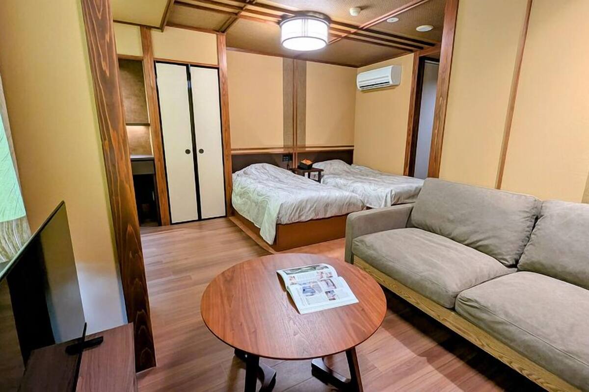 A hotel room with a bed, a sofa, a small table with a magazine, and a TV.