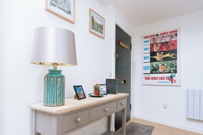 A room with a desk, a lamp, framed pictures, and a poster on the wall.