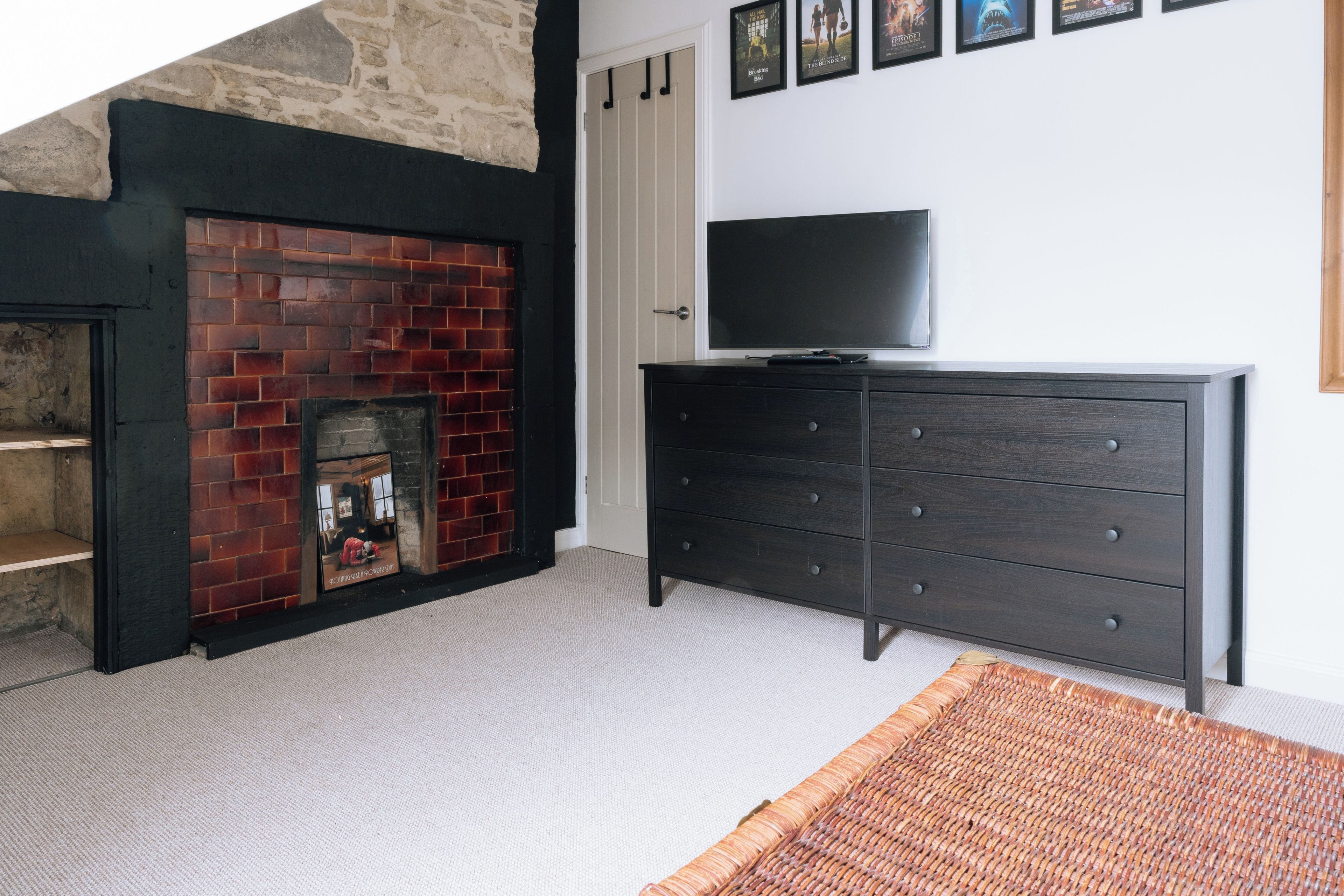 A room with a brick fireplace, a flat-screen TV on a dresser, and a woven rug on the floor.