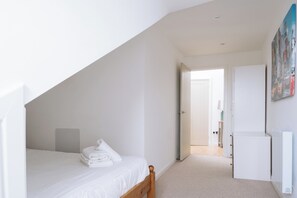A bedroom with a sloped ceiling, a bed with white linens, a radiator, and a door leading to another room. - Charming Flat in the Heart of Edinburgh Old Town (Edinburgh)