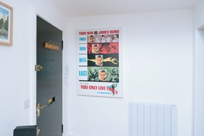 A room with a door leading to a hallway, a coat rack, and a poster on the wall.