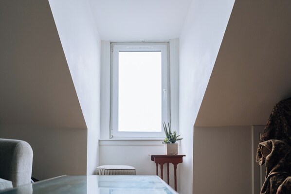 A room with a sloped ceiling, a window, a small table with a plant, and a chair. - Charming Flat in the Heart of Edinburgh Old Town (Edinburgh)