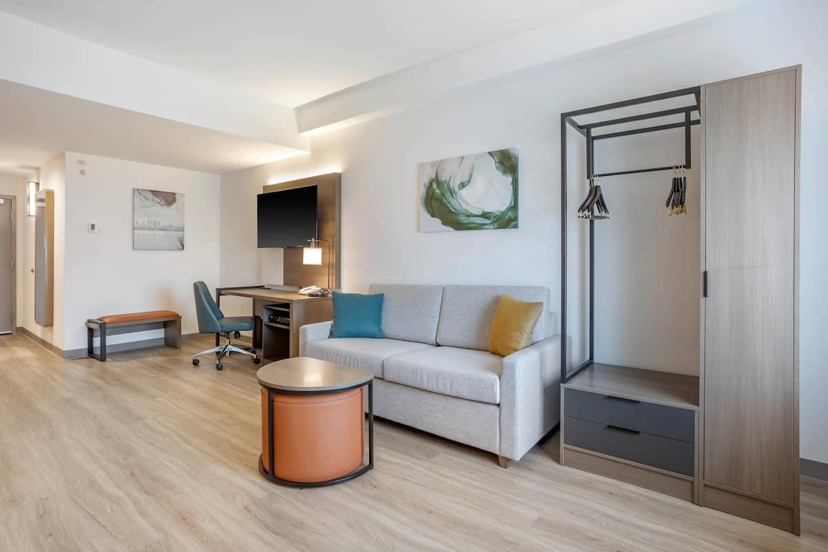 Une chambre d’hôtel moderne équipée d’un canapé, d’un bureau, d’une chaise, d’une table ronde et d’une armoire.