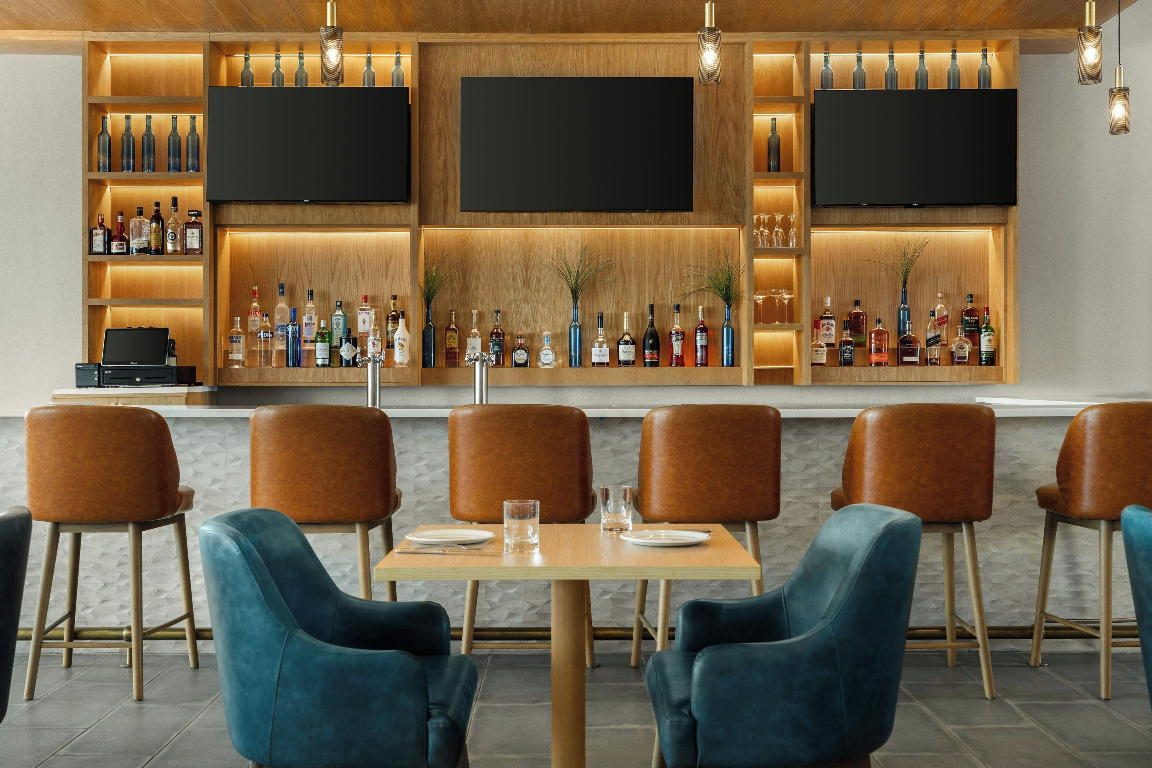 A bar area with multiple seating options, a variety of liquor bottles, and a flat-screen TV mounted on the wall.