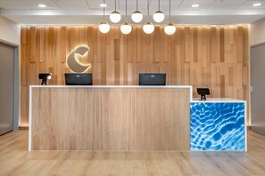 Una reception con due monitor per computer, un pannello di legno decorato con un motivo a onda e illuminazione a sospensione.
