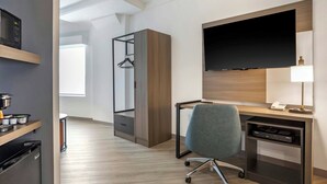 A modern hotel room with a desk, chair, TV, and a wardrobe.
