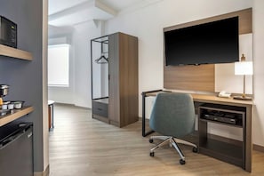 Quarto de hotel moderno com escrivaninha, cadeira, televisão e guarda-roupa.