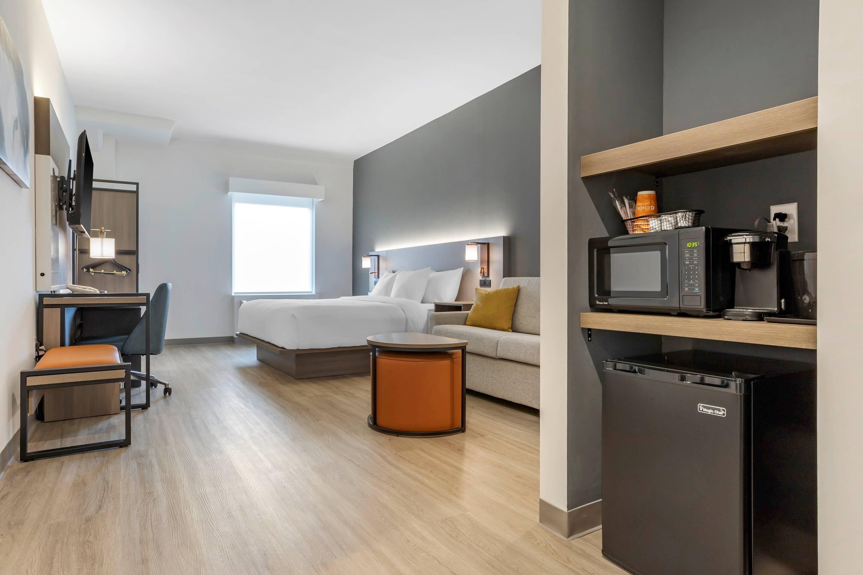 Habitació d'hotel senzilla amb llit, escriptori, cadira, taula petita, frigorífic i microones.