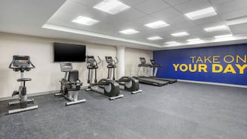 A gym with various exercise equipment, a large screen, and motivational wall text.