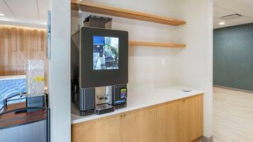 Un kiosque en libre-service doté d’un écran tactile, d’une machine à café et d’un petit réfrigérateur.