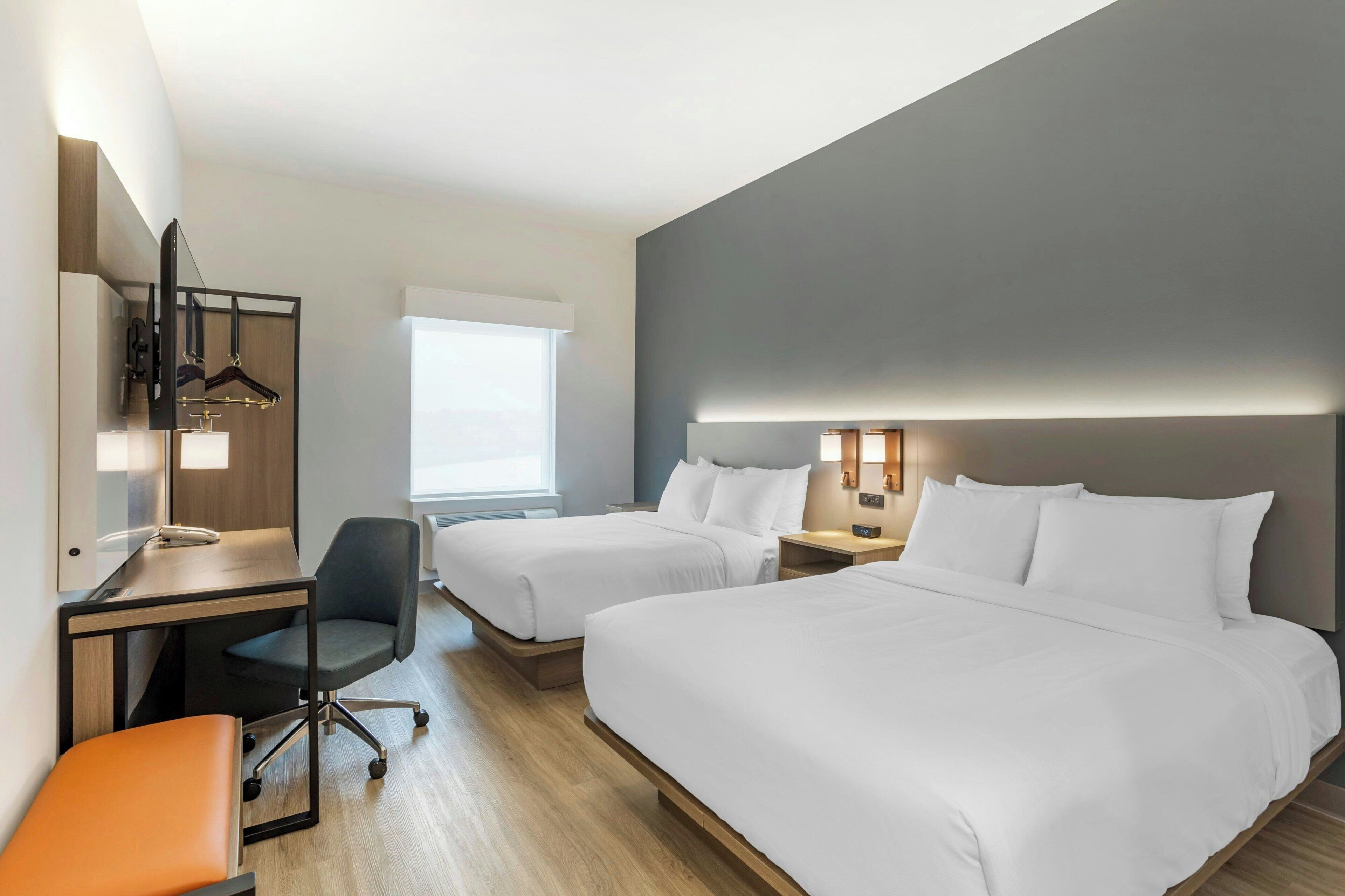A hotel room with two beds, a desk, a chair, and a mirror.