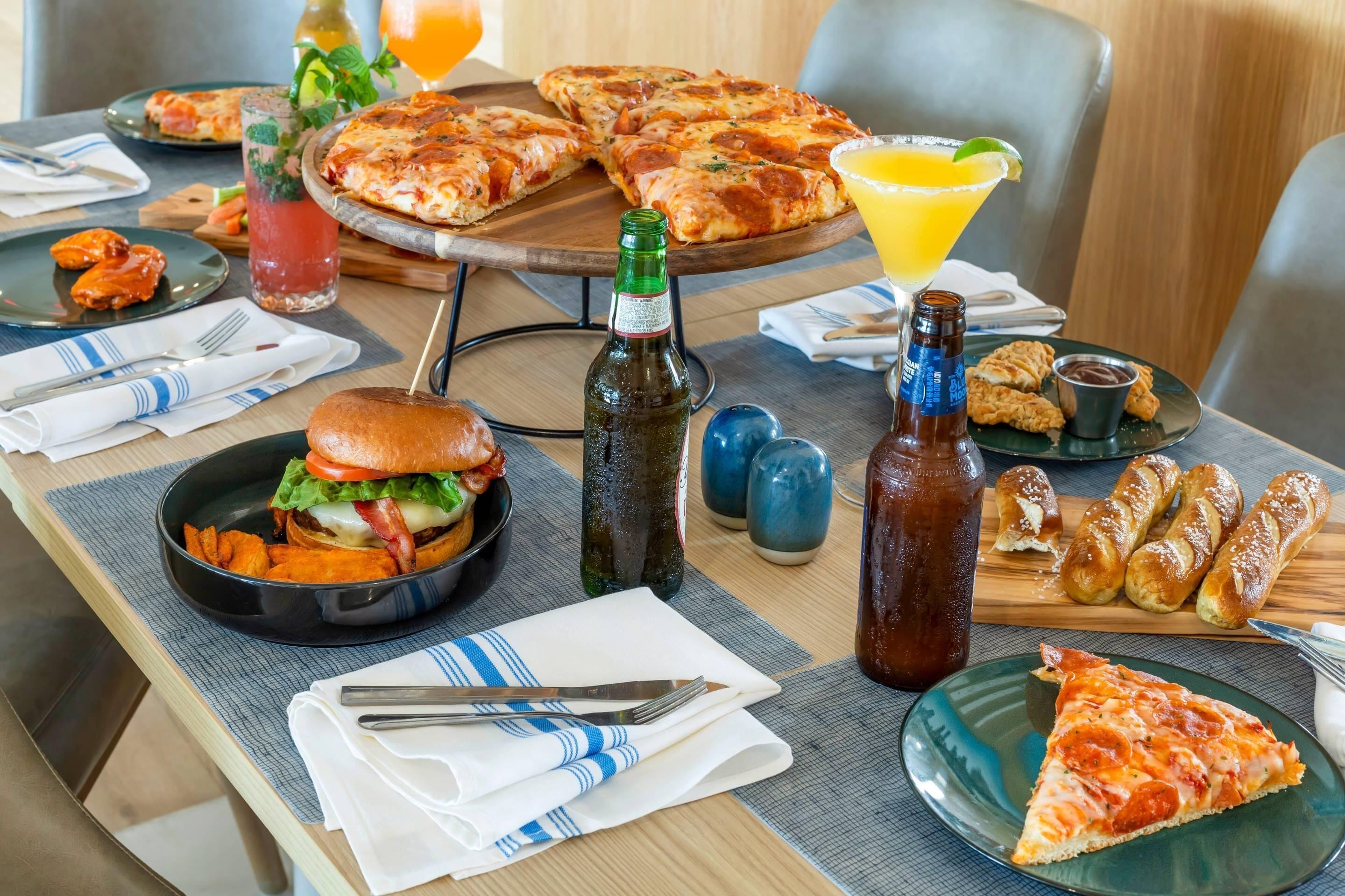 Une table à manger avec une pizza, un hamburger, un verre à martini et des condiments.