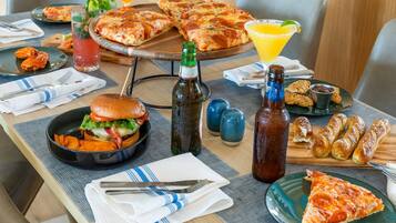 Une table à manger avec une pizza, un hamburger, un verre à martini et des condiments.