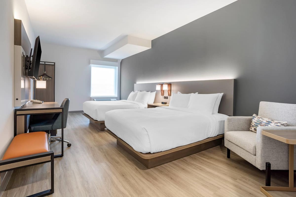 Une chambre d’hôtel moderne équipée d’un bureau, de deux lits, d’une chaise et d’un téléviseur.