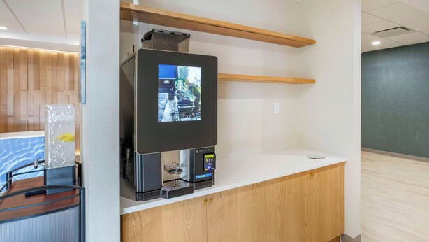 Un quiosco moderno de autoservicio con pantalla táctil, una máquina de café y un refrigerador pequeño.
