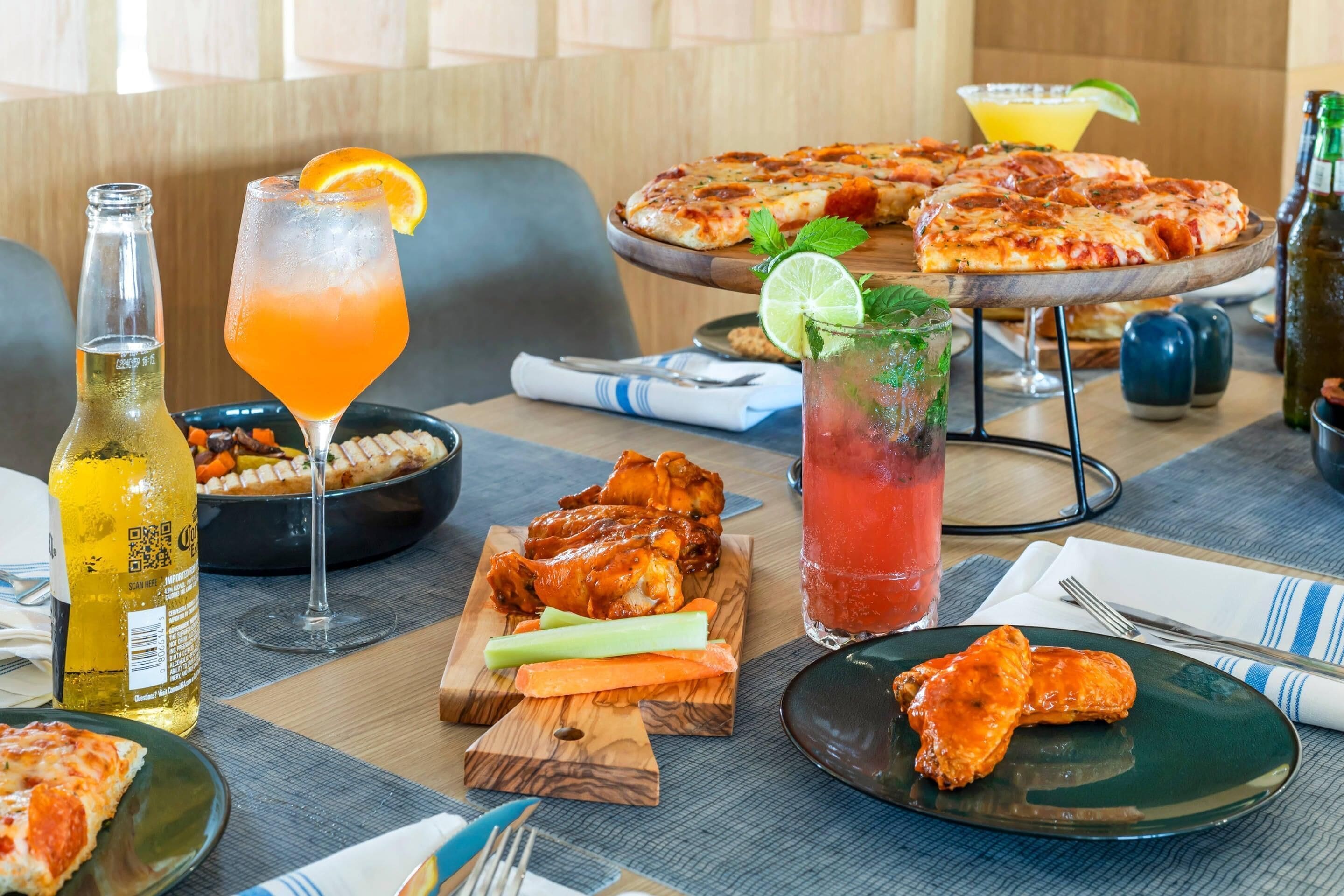A dining table with pizza, wings, and drinks.