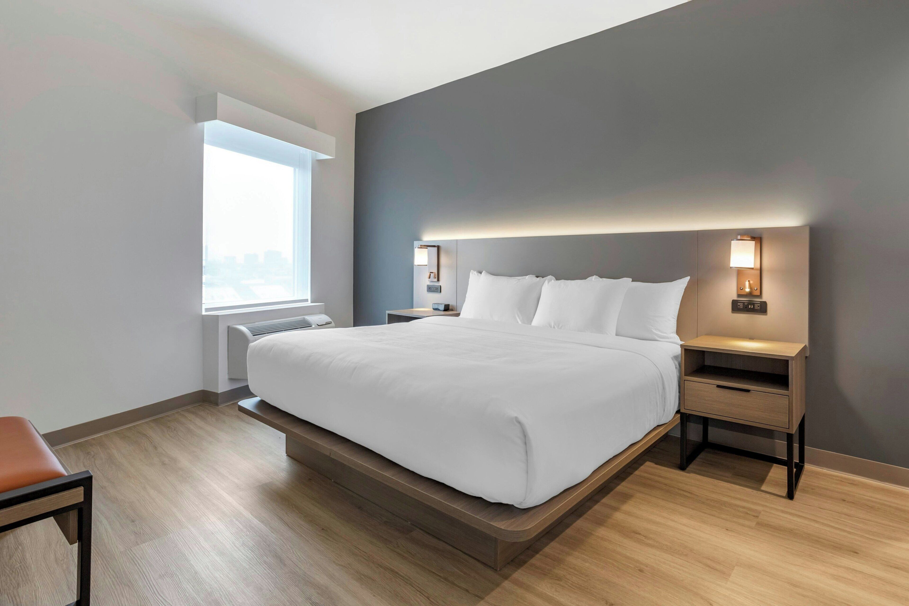 A modern hotel room with a large bed, bedside tables, a window, and a built-in heater.