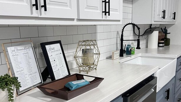 Cocina moderna con alacenas blancas, lavavajillas y encimera con una bandeja y un cartel.