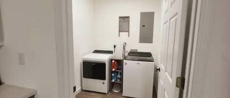 Un lavadero con lavadora y secadora, un estante pequeño con productos de limpieza y una puerta a otra habitación.