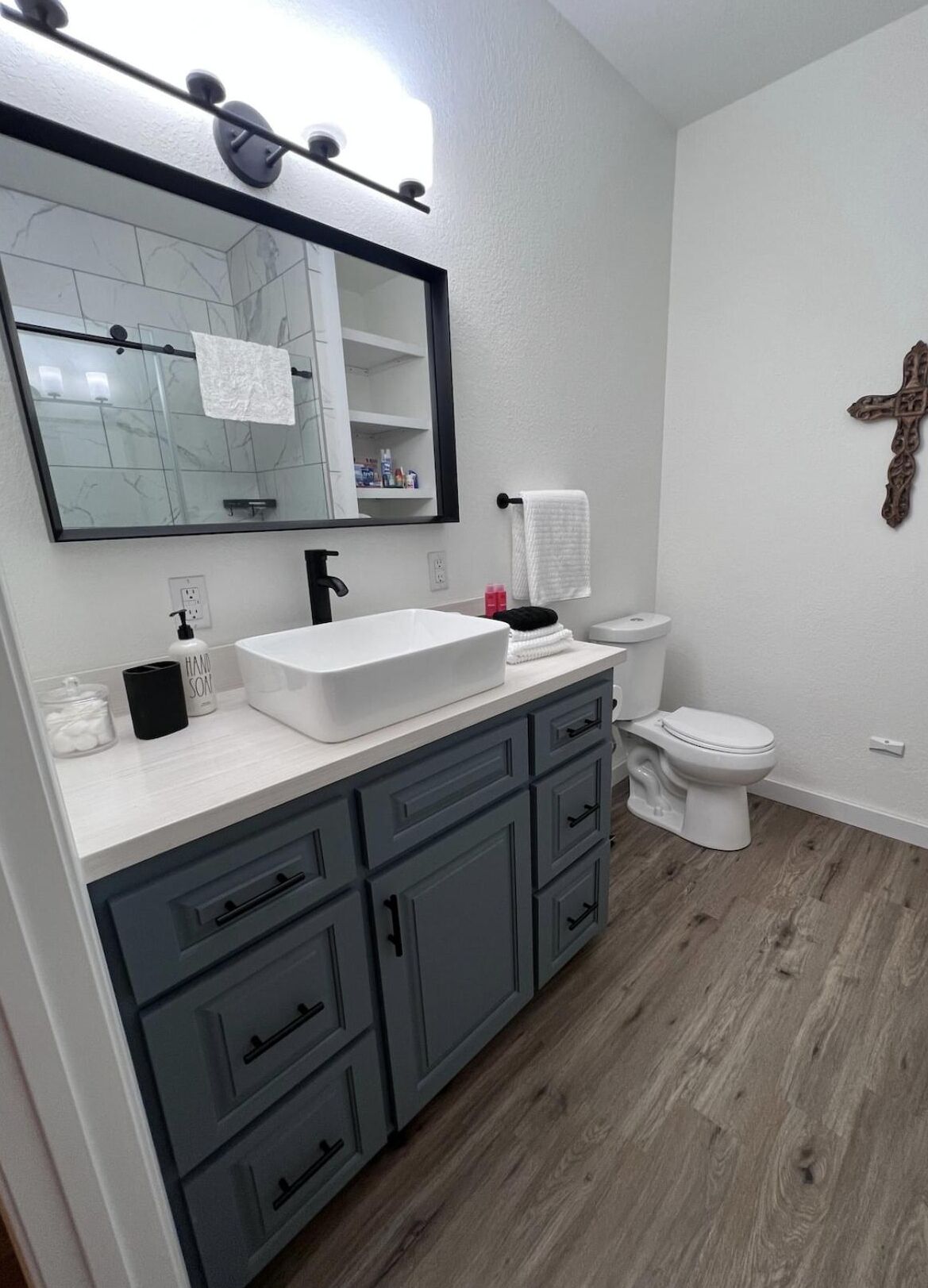 Een moderne badkamer met een witte wastafel, donkergrijze kastjes, een grote spiegel en een wit toilet.