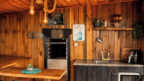 Un interior rústico de madera con un horno de leña, una zona de bar con lavamanos y distintos utensilios de cocina.