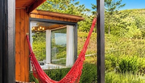 A wooden structure with a glass window and a red hammock. - Refúgio Serra da Tartaruga (Alfredo Wagner)