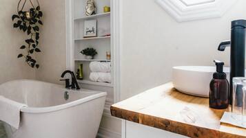 A modern bathroom with a freestanding bathtub, a white sink with a black faucet, and a wooden countertop.