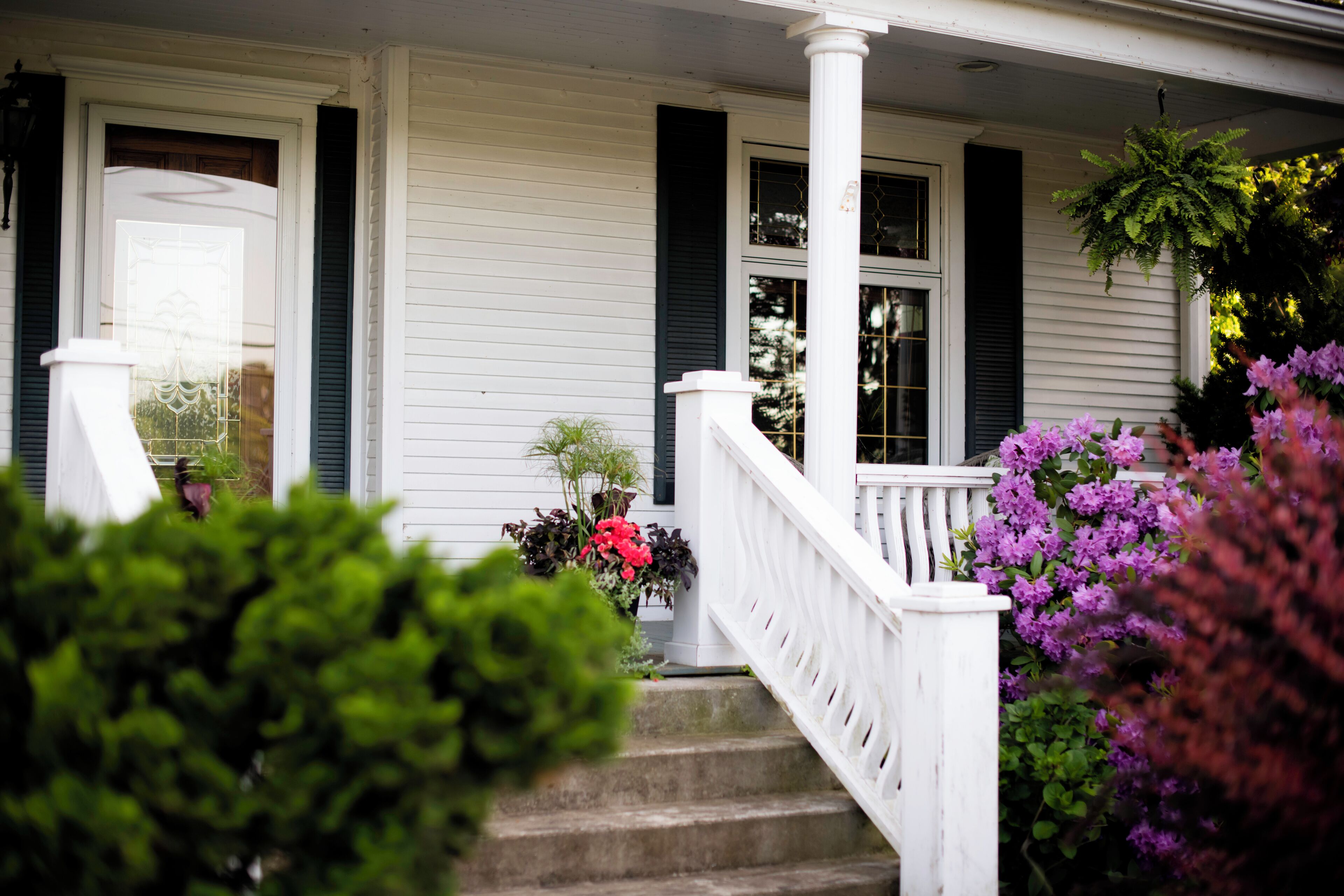 A white porch with a white railing, steps, and a door with a window.