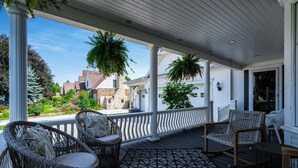 A covered porch with wicker chairs, a patterned rug, and hanging plants. - Dream Estate Inn (Leamington)