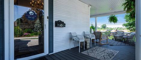 A covered porch with outdoor seating, a welcome sign, and a view of the landscape.