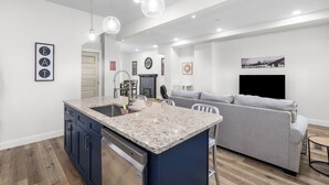 Una cucina moderna con piani in granito, lavastoviglie integrata e illuminazione a sospensione.