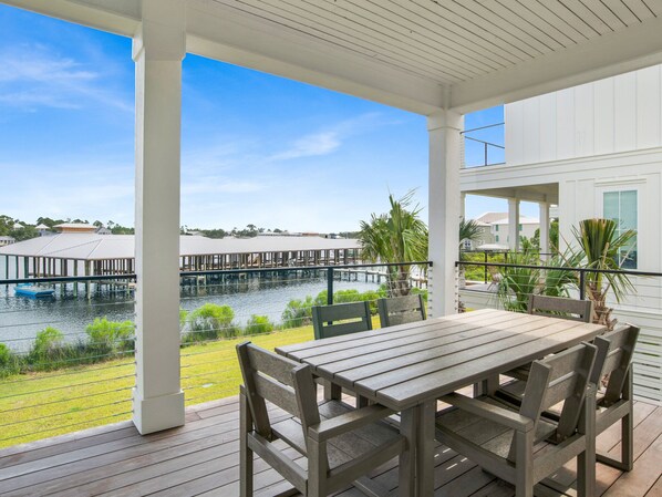 A covered outdoor area with a wooden table and chairs, overlooking a water body with docks and buildings in the background. - The Osprey by Southern Vacation Rentals (Orange Beach)