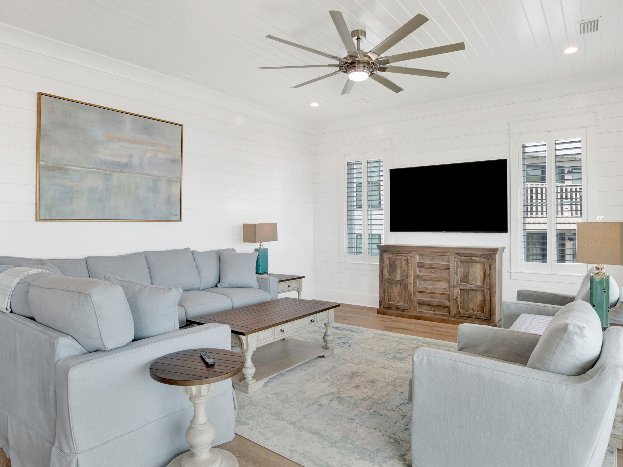 A spacious living room with a grey sofa, a wooden coffee table, a TV, and a ceiling fan.