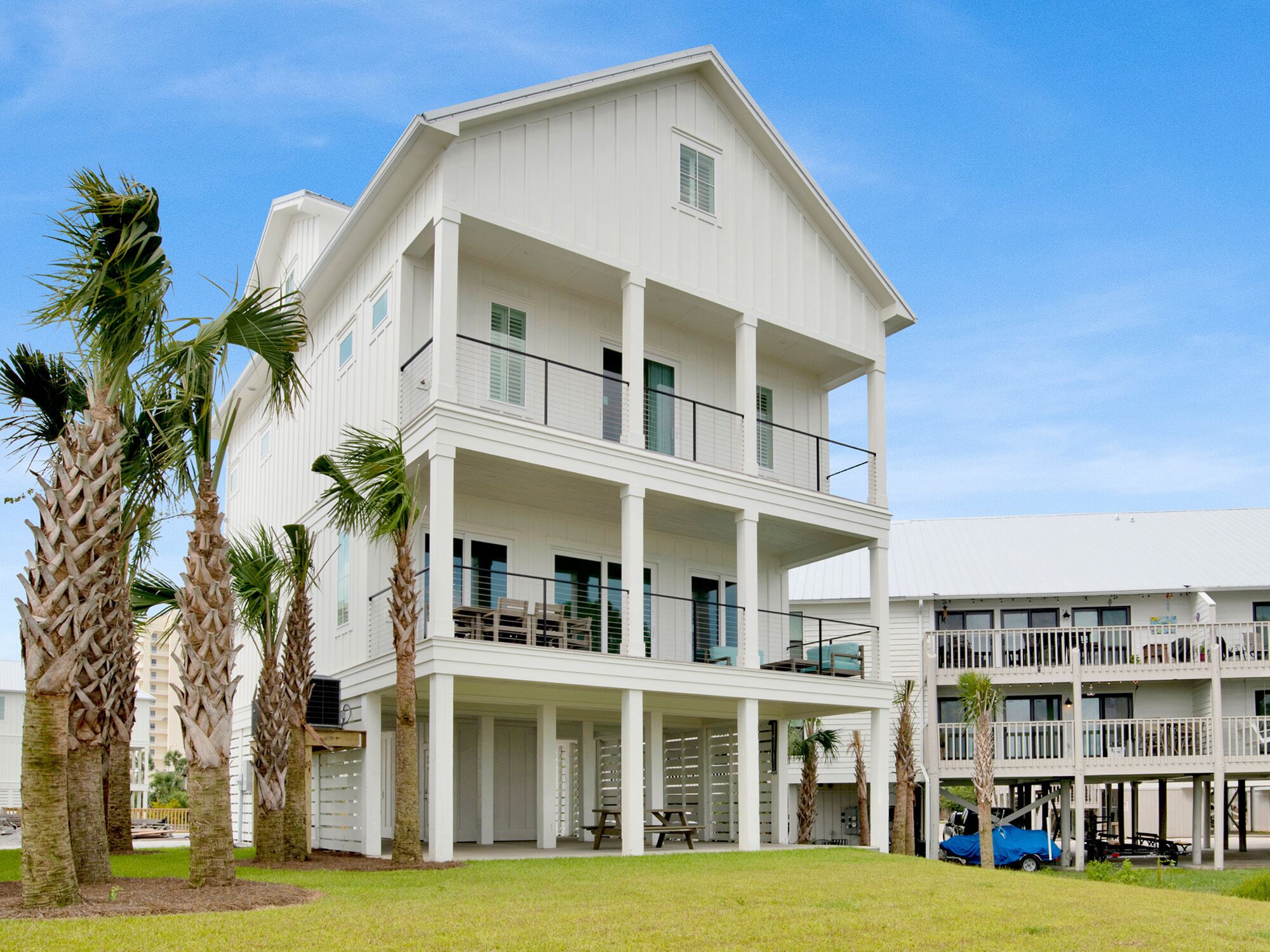 A multi-story white building with balconies, palm trees, and a clear blue sky.