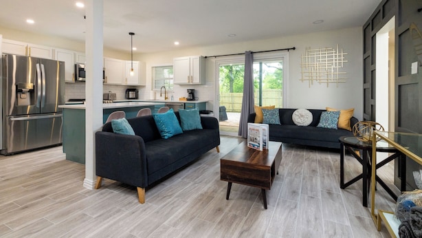 A modern kitchen with stainless steel appliances, a dining area with a dark sofa and coffee table, and a living area with a dark sofa and decorative pillows. - Walk to Marina Park + Sleeps 8 - Near Stockyards (Lake Worth)
