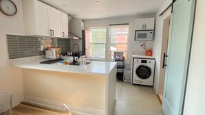 A modern kitchen with white cabinetry, a large island, a built-in microwave, and a washing machine. - PET friendly - Sunny 1 Bedroom Apartment , (Grimsby)