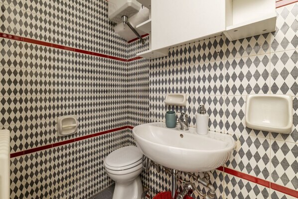 Une salle de bain avec un mur recouvert de carreaux disposés en motif losange, un lavabo blanc et des toilettes.