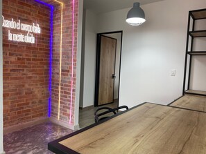 Een kamer met een bakstenen muur, een neonbord, een houten deur en een tafel met stoelen.