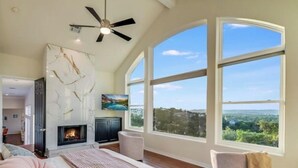 A spacious bedroom with a fireplace, large windows, and a view of the landscape. - Paradise on Lake Travis (Austin)