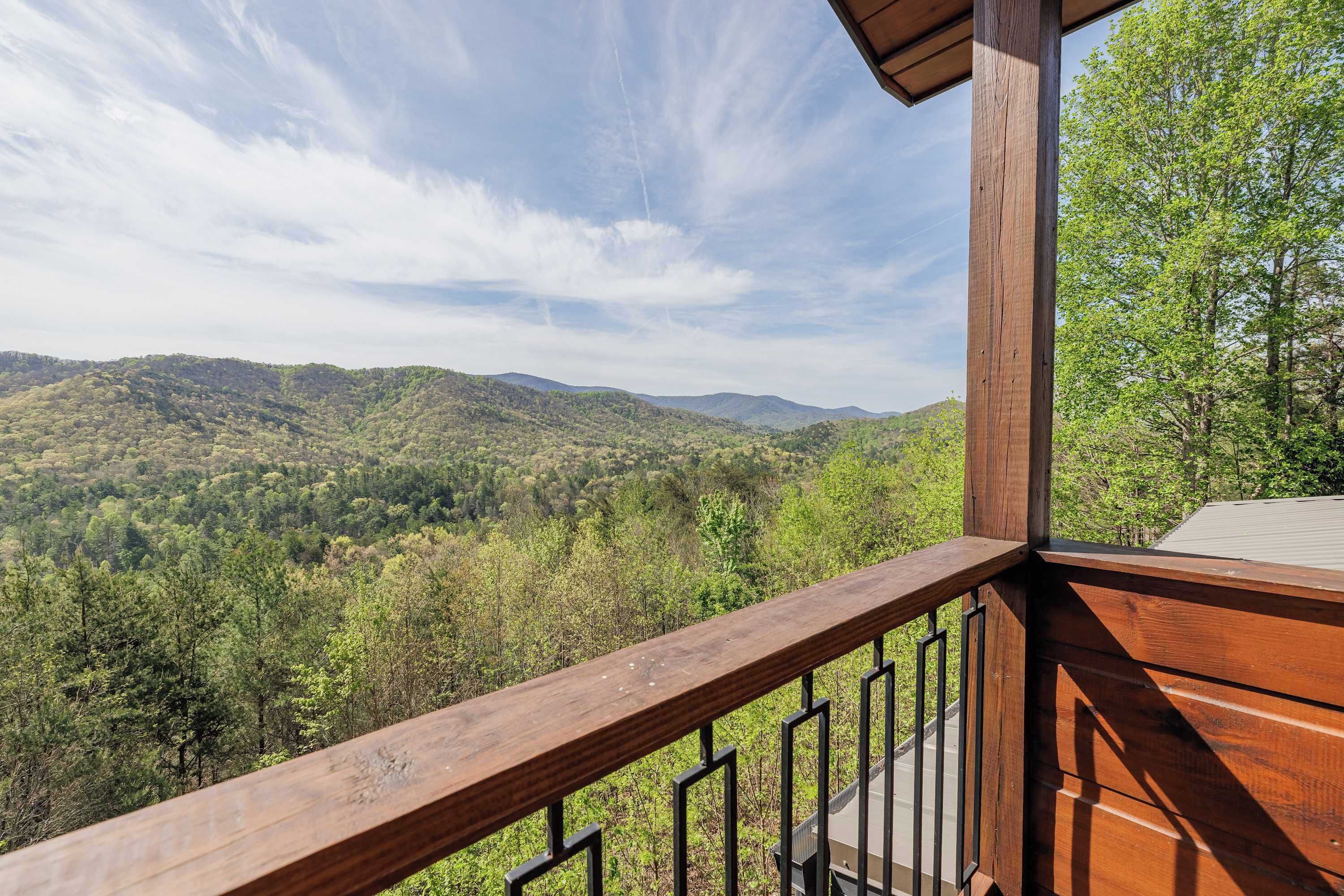 Un balcon en bois, doté d’une rambarde en métal, qui offre une vue sur un paysage montagneux boisé.