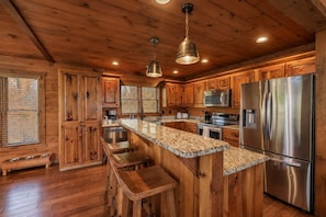 A kitchen with wooden cabinets, a stainless steel refrigerator, and a granite countertop. - Family Mountain Cabin in Blue Ridge, GA | Prime Fall Leaf Views1 (Blue Ridge)
