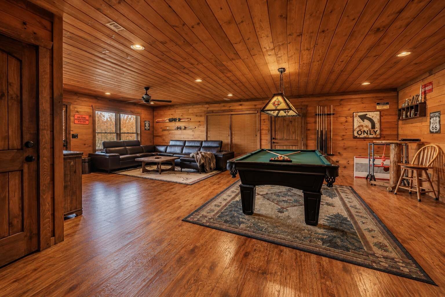 A wooden interior with a pool table, leather sofa, and a ceiling fan.