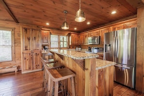 Une cuisine rustique, située dans une cabane en bois, avec un îlot central, des tabourets de bar, des appareils électroménagers en acier inoxydable et des armoires en bois.