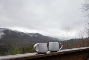 Two white ceramic mugs on a wooden ledge with a mountainous landscape in the background. - Family Mountain Cabin in Blue Ridge, GA | Prime Fall Leaf Views1 (Blue Ridge)